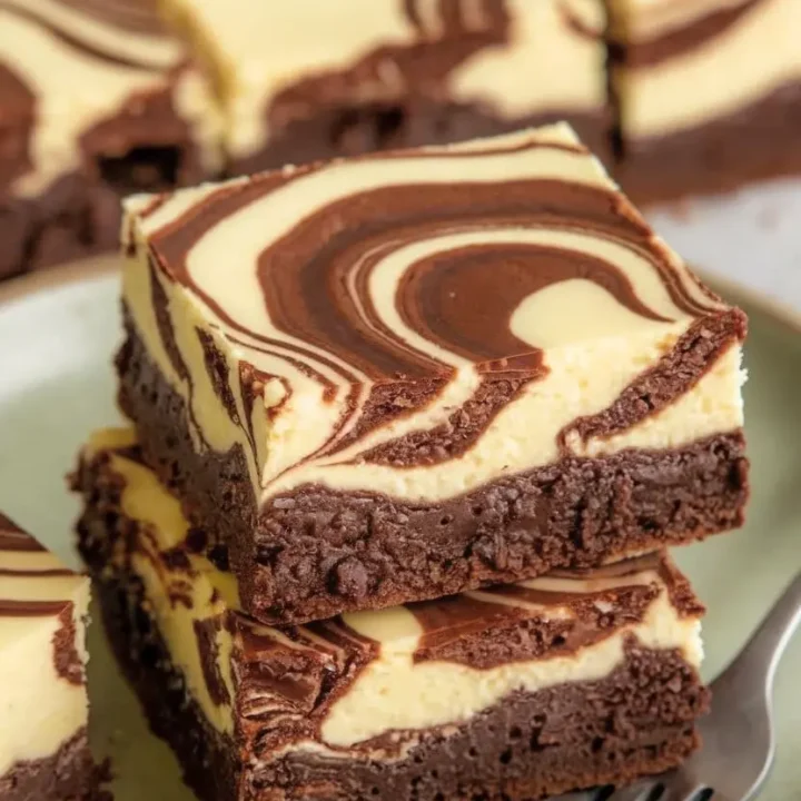 Rich Cheesecake Brownies with swirled chocolate on top. on light green plate and a fork.