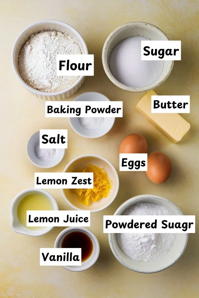 Ingredients for lemon brownies on a light-yellow surface including flour,sugar, baking powder, butter, salt, eggs, lemon zest, powdered sugar, fresh lemon juice, and vanilla.