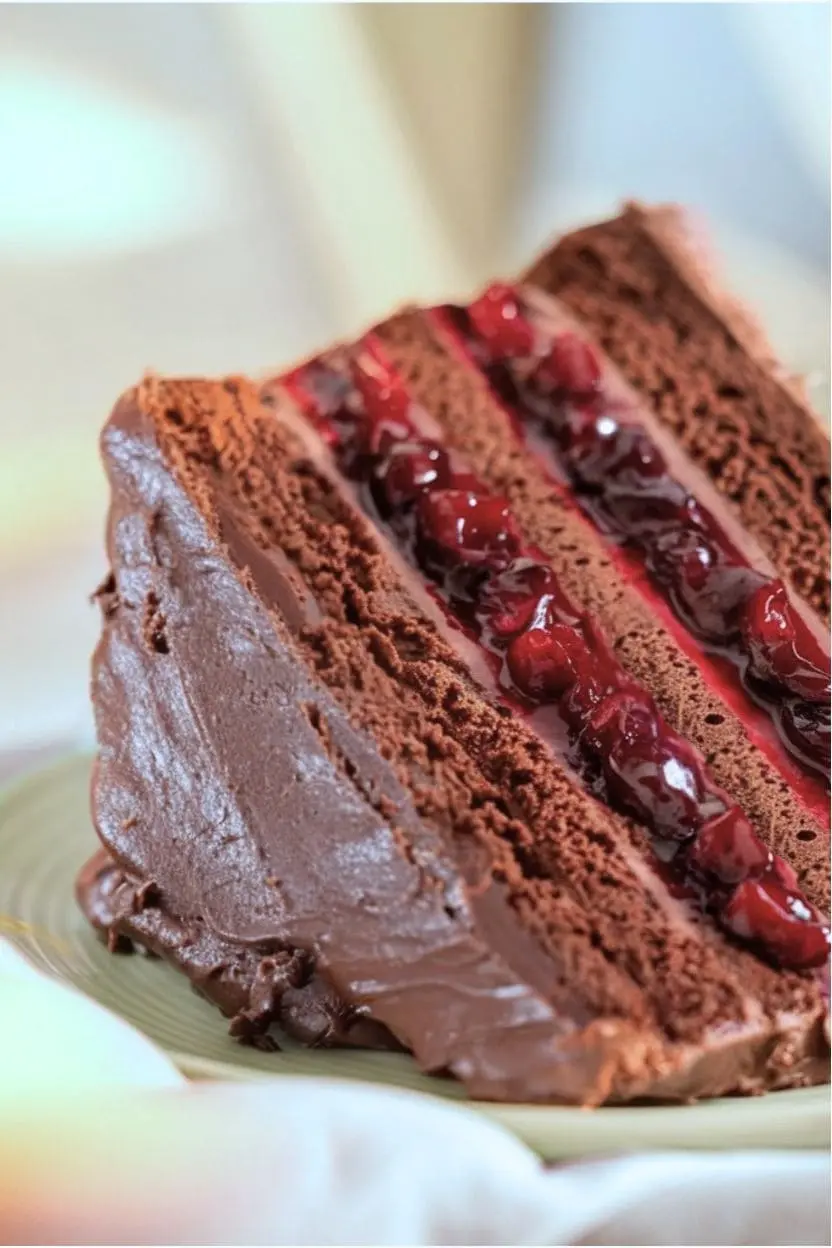 slice of a chocolate cherry cake on a light green plate showing the juicy cherry filling between the cake layers.