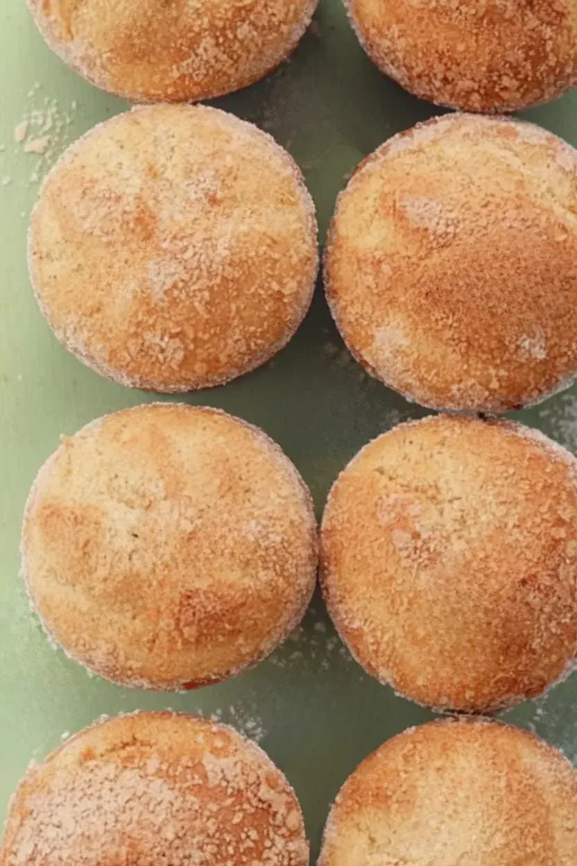 A top-down view of a freshly baked vegetarian cinnamon sugar donut muffin resting on a light green surface coated with cinnamon sugar.