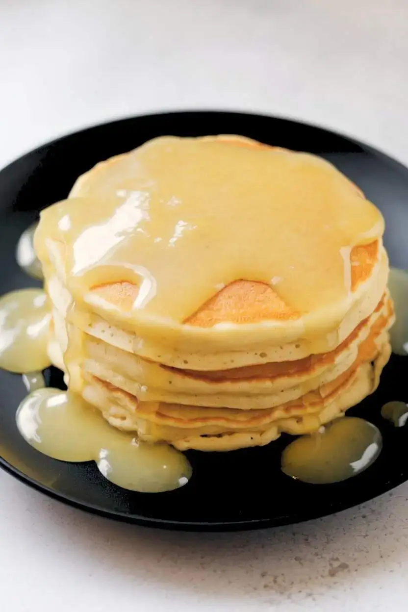 Lemon compote drizzled over pancakes on a black plate.