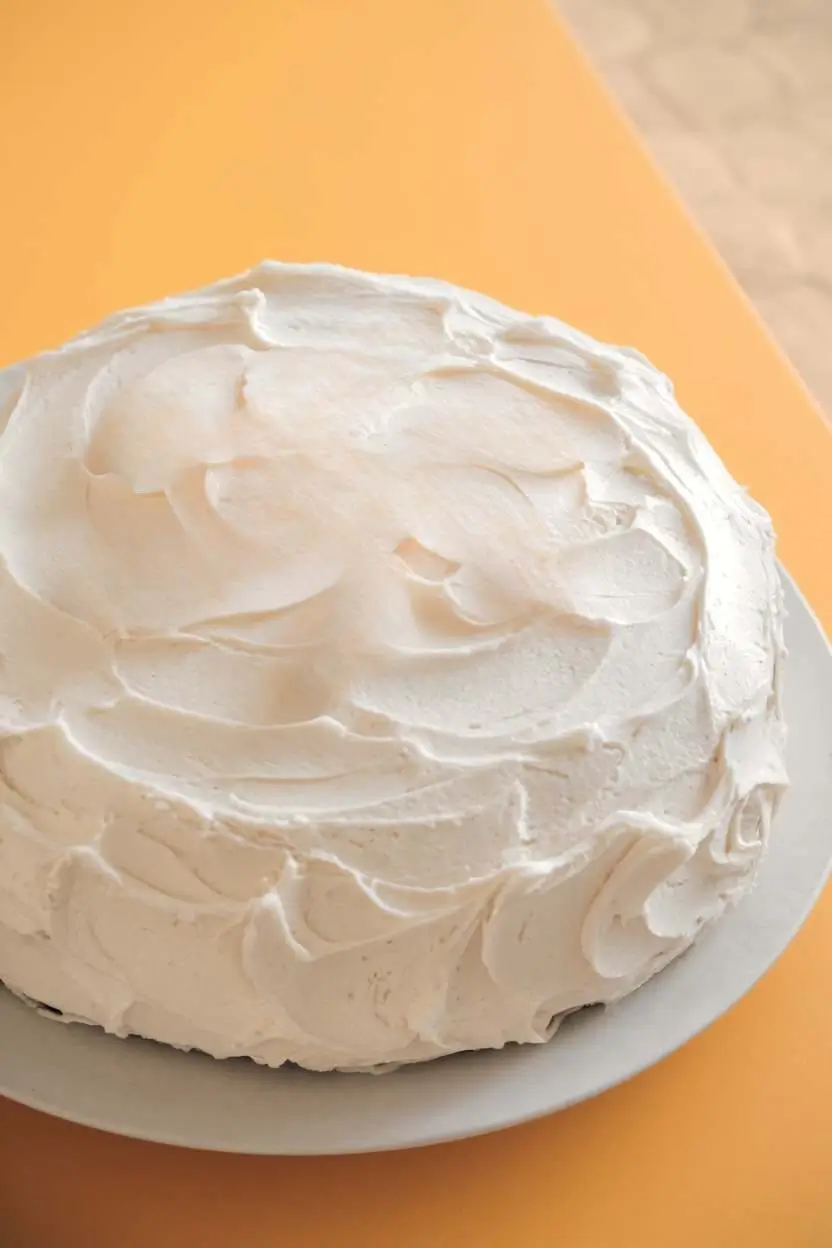 Mandarin orange cake with only the frosting rests on a white plate against a light orange surface.